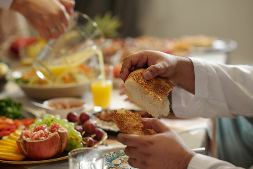 en manns hender bryter et stykke brød i to ved et bord fylt av mat.