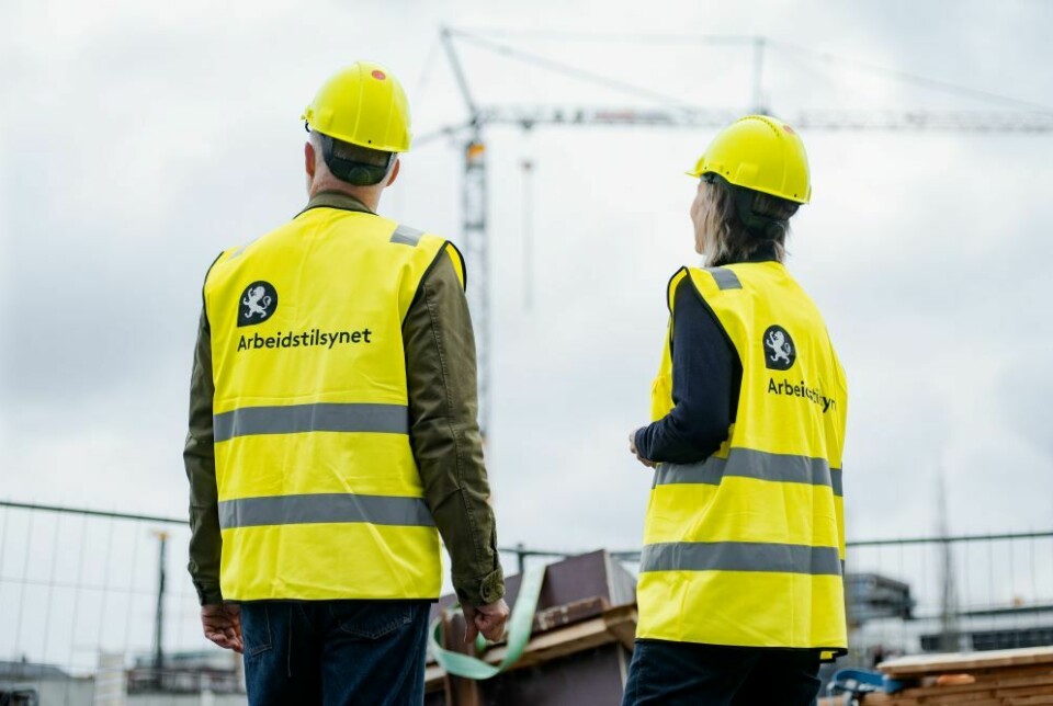 mann og kvinne på byggeplass med vernehjelm og refleksvest med Arbeidstilsynets logo på